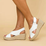 White wedge sandals with jute sole worn by a person on a beige background