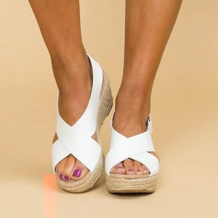 White wedge sandals with jute sole worn by a person on a beige background
