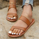 Brown sandals worn on feet with white nail polish, standing on a stone surface.