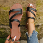 Black strappy sandals worn with ripped jeans against a stone wall background