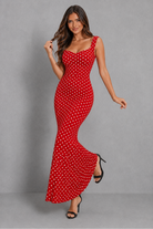 A woman modeling a red sleeveless maxi dress with a white polka dot pattern against a solid gray studio background.