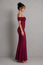 Woman wearing a burgundy off-shoulder lace dress against a gray background