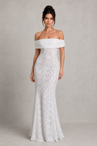 Woman wearing a white off-shoulder lace gown against a plain background
