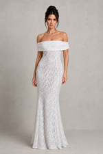 Woman wearing a white off-shoulder lace gown against a plain background