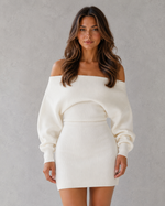 Woman wearing a white off-shoulder sweater dress against a gray background