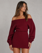 Woman wearing a burgundy off-shoulder sweater dress against a gray background