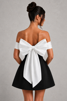 Woman wearing a black dress with a large white bow at the back on a gray background