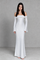 Woman wearing a white off-shoulder dress with long sleeves against a gray background