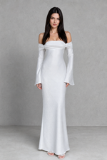 Woman wearing a white off-shoulder dress with long sleeves against a gray background