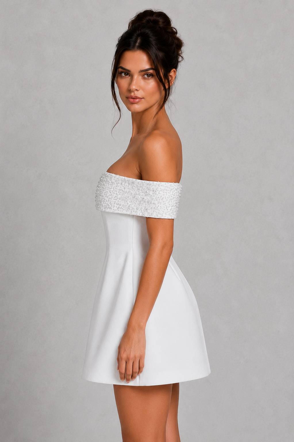Woman wearing a white off-shoulder dress with sequin top on a gray background