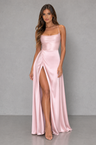 Woman wearing a pink satin dress with a high slit on a gray background