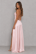 Woman wearing a pink evening gown with a backless design against a gray background