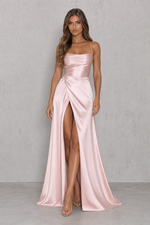 Woman wearing a pink satin gown with a high slit on a gray background