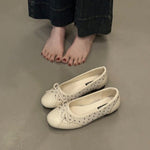 White shoes with lace-up design on a gray floor, next to a person wearing dark pants.