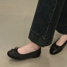 Black studded flats worn with black pants on a neutral background