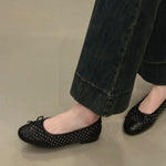 Black studded flats worn with black pants on a neutral background
