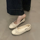 White flat shoes worn with dark jeans on a neutral floor.