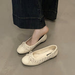 White flat shoes worn with dark jeans on a neutral floor.