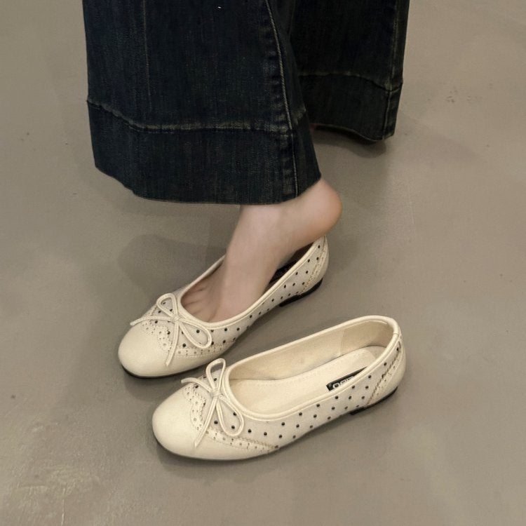 White flat shoes worn with dark jeans on a neutral floor.