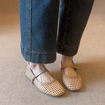 Person wearing beige woven flats with rolled-up jeans on a neutral carpeted floor.