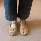 Person wearing beige mesh shoes with dark jeans on a neutral carpeted floor
