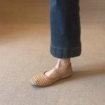 Person wearing a woven sandal on a beige carpet