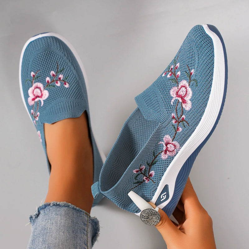 Blue slip-on shoes with floral embroidery on a gray background