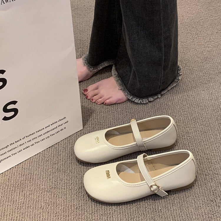 White shoes with a strap on a carpeted floor next to a white box.