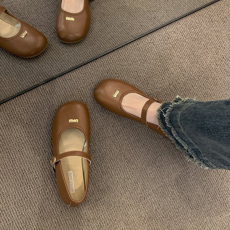 Brown shoes with 'Miu' logo worn by a person on a carpeted floor.