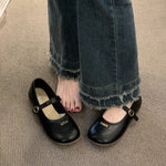 Black shoes with gold accents worn with blue jeans on a beige carpet.