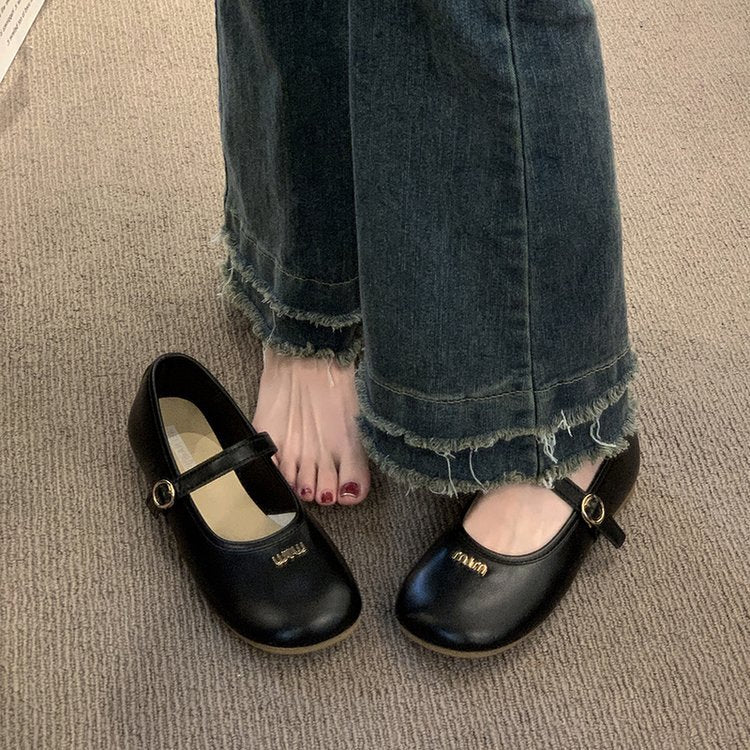 Black shoes with gold accents worn with blue jeans on a beige carpet.