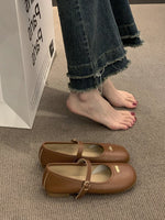 Brown shoes on a carpeted floor with a person wearing jeans in the background.