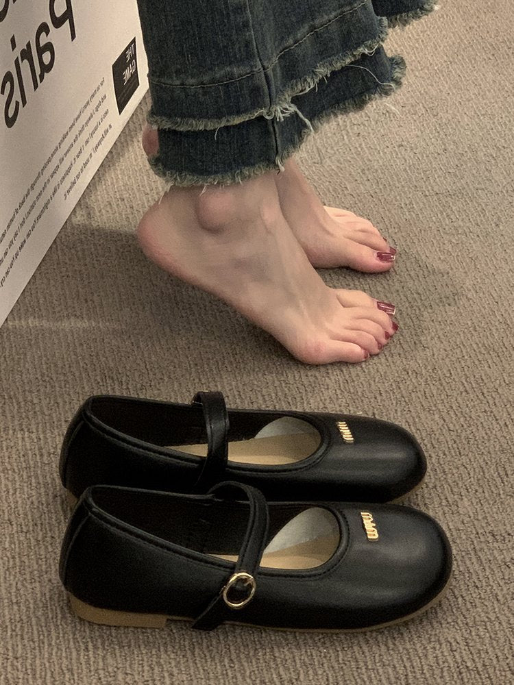 Black shoes with a strap on a carpeted floor next to a person's feet.