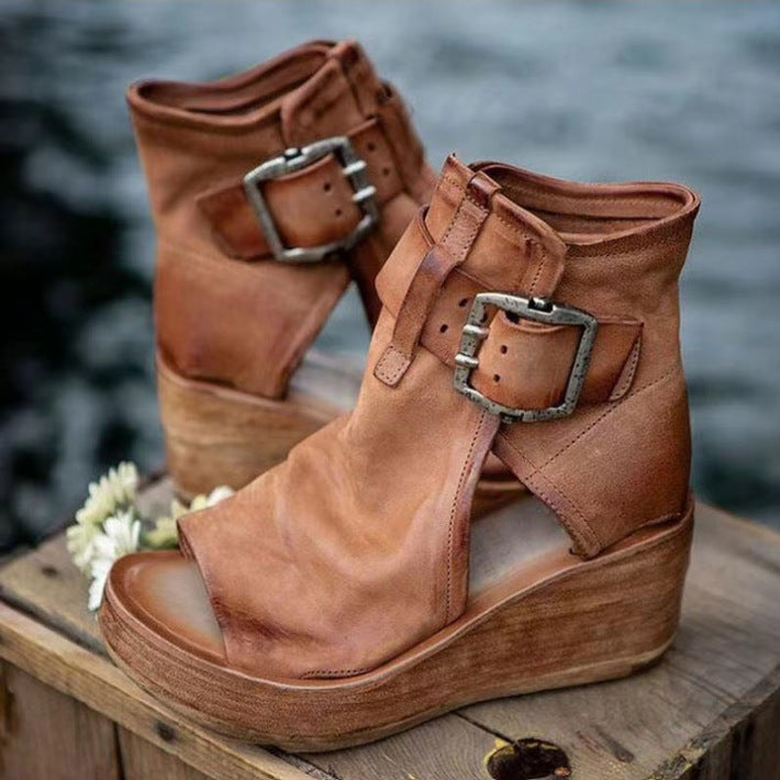 Pair of brown wedge boots with buckles on a wooden surface with a blurred natural background