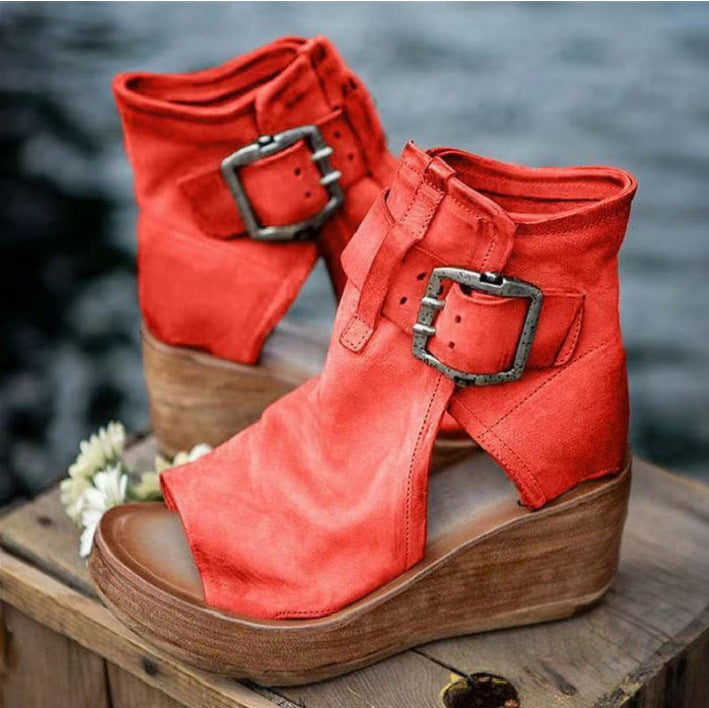 Red wedge sandals with buckles on a wooden surface with a blurred natural background