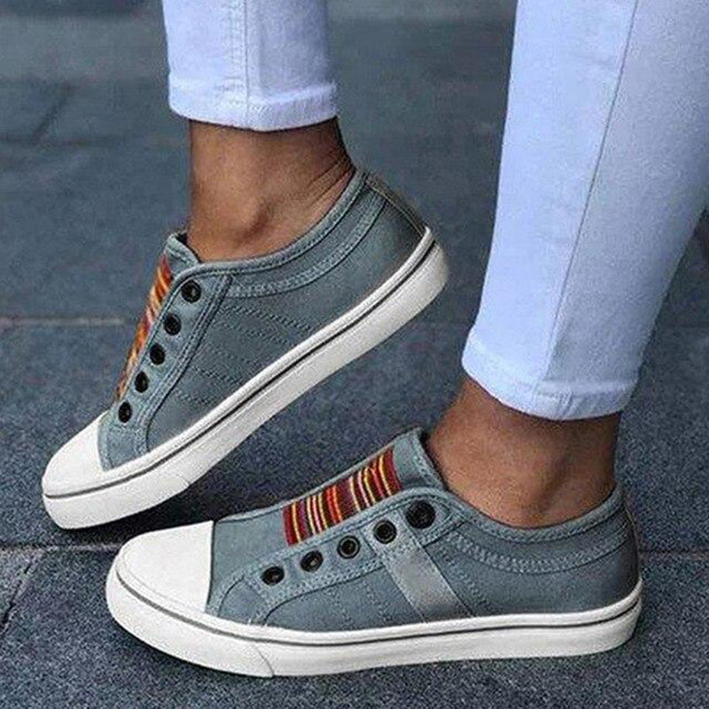 Gray slip-on sneakers with colorful accents worn by a person on a gray pavement.