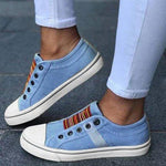 Light blue sneakers with colorful accents worn by a person on a gray pavement.