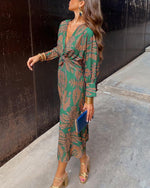 Woman in a green patterned dress standing against a black wall.