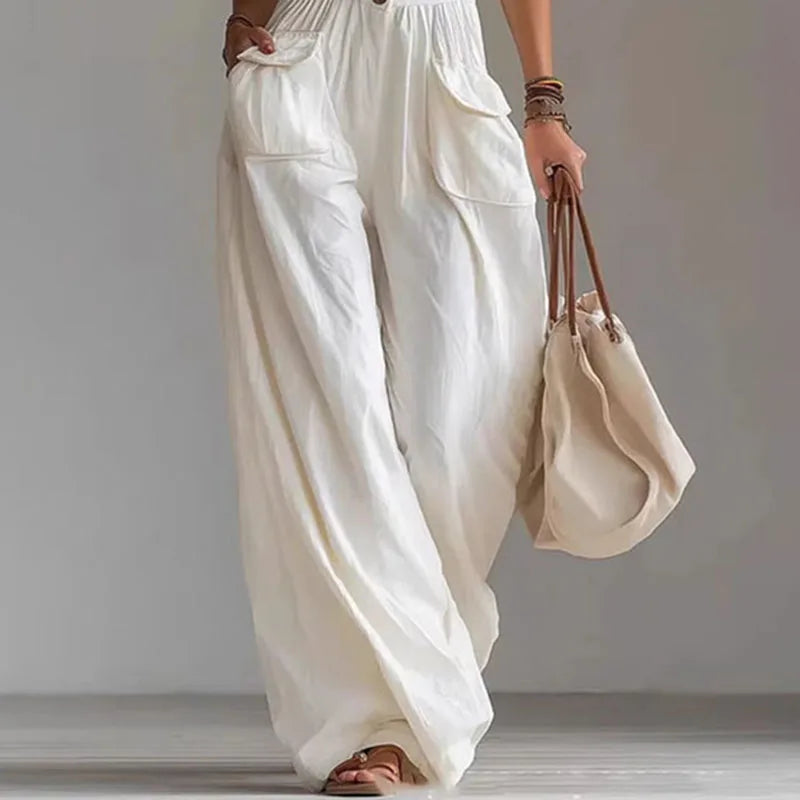 Person wearing white wide-leg pants holding a beige bag against a plain background