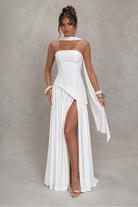 Woman wearing a white strapless gown with a slit on a gray background