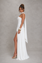 Woman wearing a white one-shoulder dress with a slit on a gray background