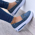 Blue sneakers with white soles worn on a light wooden floor.