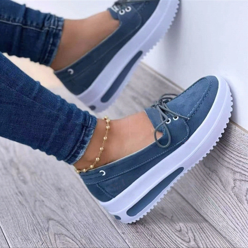 Blue sneakers with white soles worn on a light wooden floor.