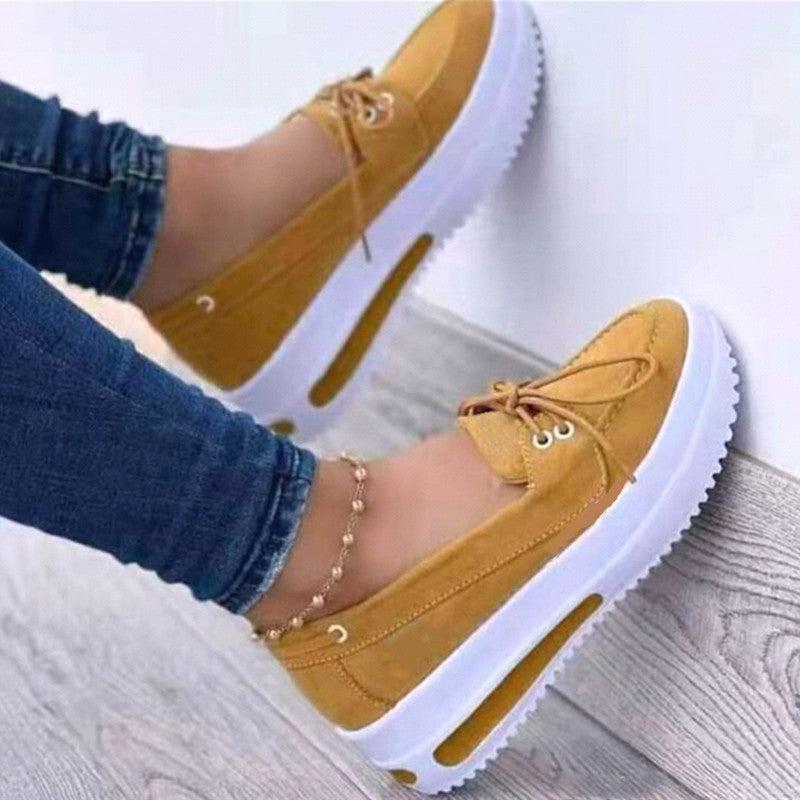 Yellow loafers with white soles worn by a person on a light wooden floor.