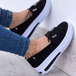 Black platform shoes with white soles worn with blue jeans on a light wooden floor.