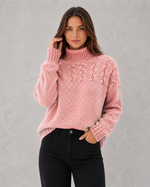 Woman wearing a pink cable knit sweater against a gray background