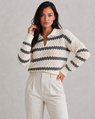 Woman wearing a striped sweater and white pants against a gray background