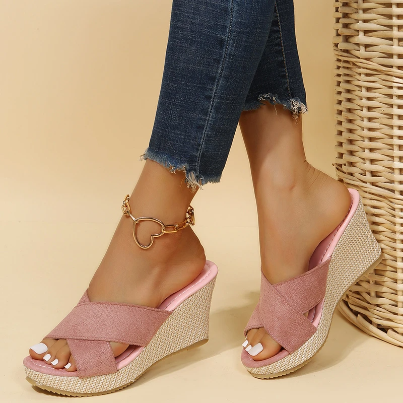 Pink wedge sandals worn with blue jeans against a beige background