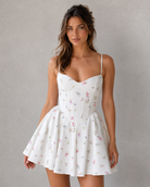 Woman wearing a white floral dress against a gray background