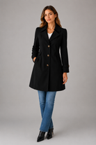 Woman wearing a black coat, blue jeans, and black shoes on a gray background